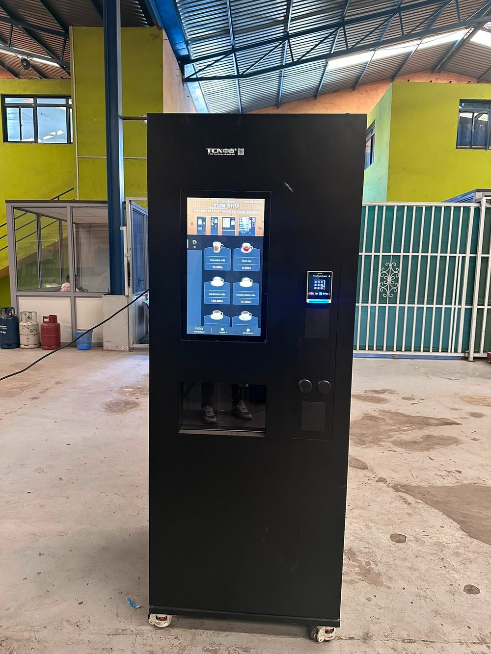 A Vendlite coffee vending machine with a large touchscreen menu showing chocolate milk, black tea, cardamom latte and masala chai latte, with a contactless card reader beside it
