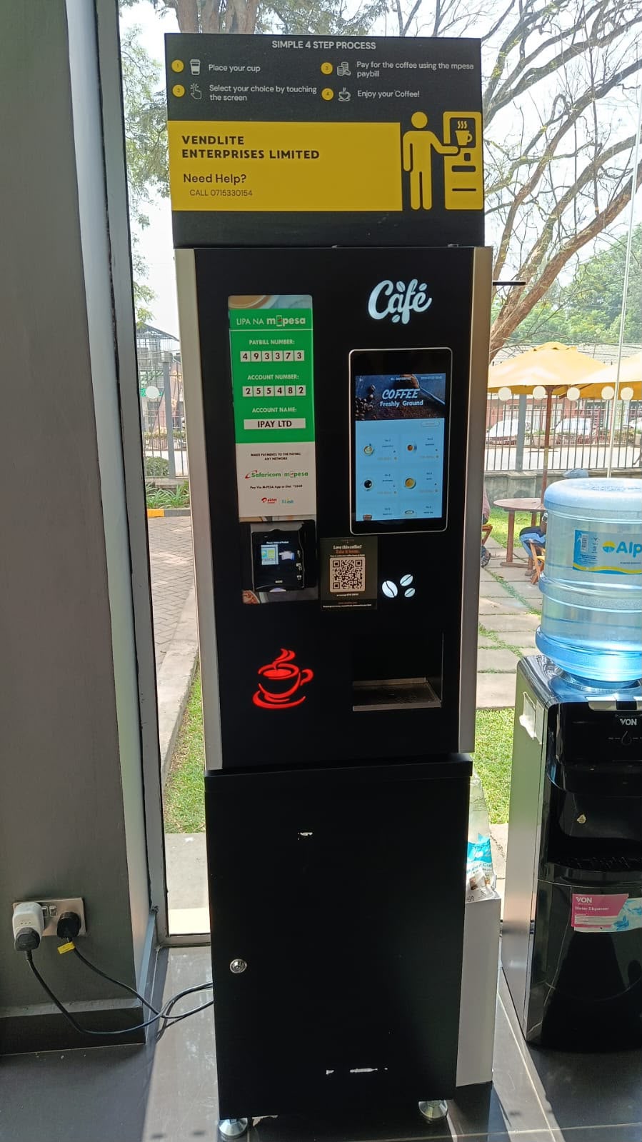 A Vendlite coffee vending machine serving freshly ground coffee, with M-Pesa payment details on the front